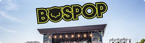 Menigte op een zonnig openluchtmuziekfestival, met een groot podium met felle lichten en schermen. Het logo van “Bospop” verschijnt boven het podium. Energieke sfeer