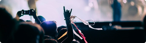 Publiek bij een concert met silhouetten van bandleden op het podium. Een hand op de voorgrond maakt het ‘rock on’-gebaar, met kleurrijke linten eraan vastgemaakt